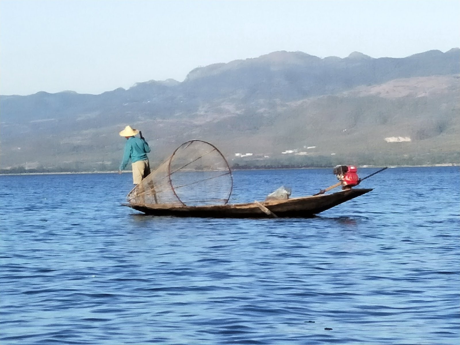 An Intha fisherman on his canoe with his leg-paddle and conical fishing net. Inle Lake, Myanmar.